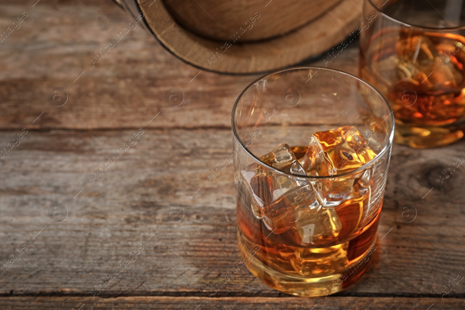 Photo of Golden whiskey in glass with ice cubes on wooden table. Space for text