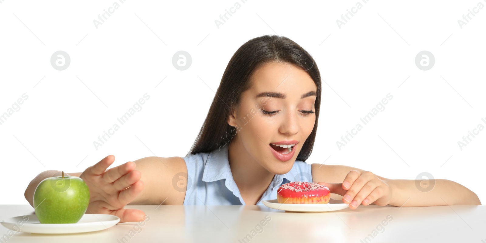 Photo of Woman choosing between apple and doughnut at table on white background