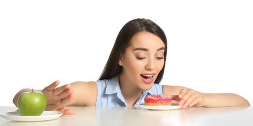 Photo of Woman choosing between apple and doughnut at table on white background