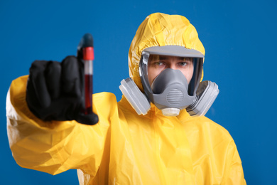 Man in chemical protective suit holding test tube of blood sample on blue background. Virus research