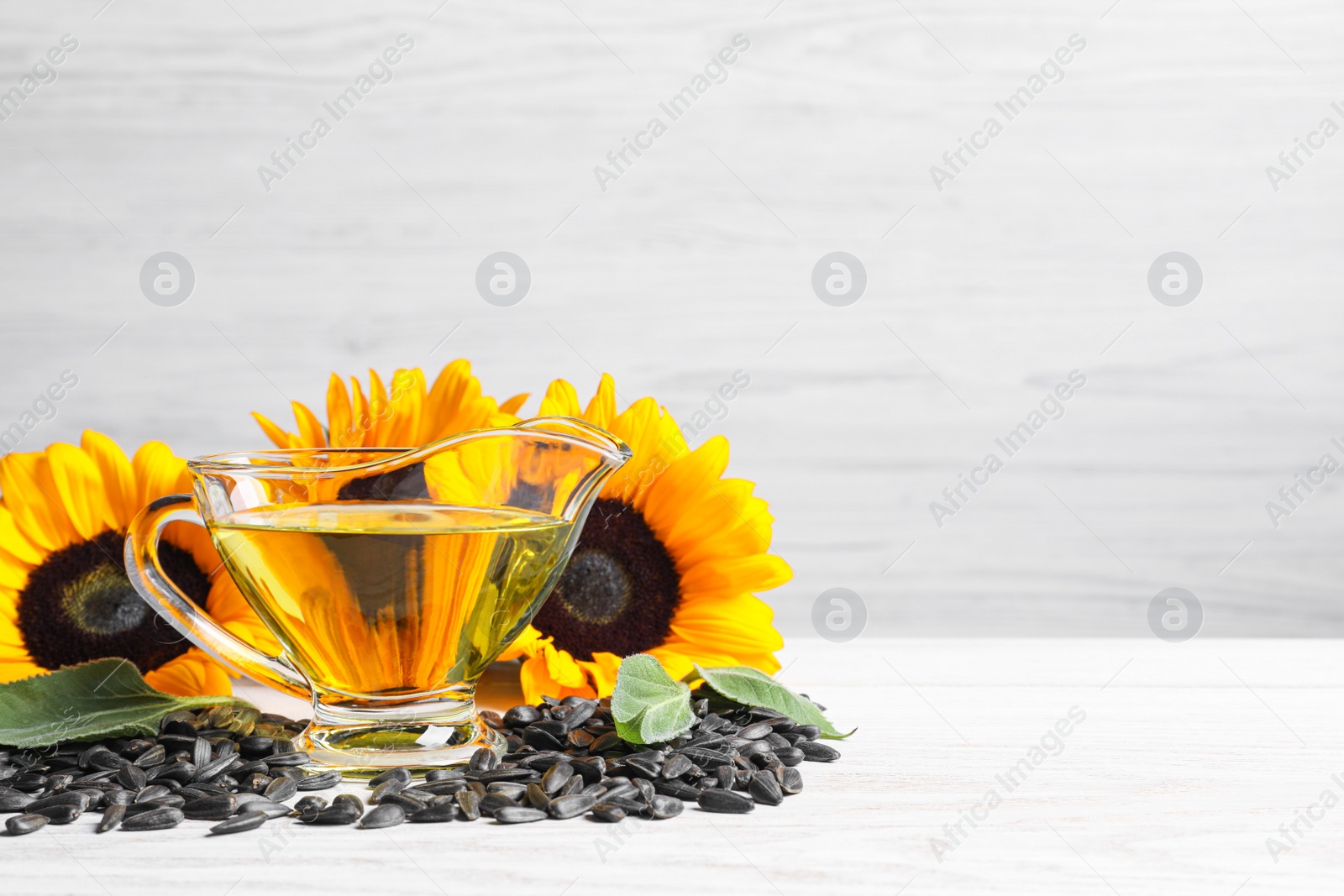 Photo of Sunflower cooking oil, seeds and yellow flowers on white wooden table, space for text