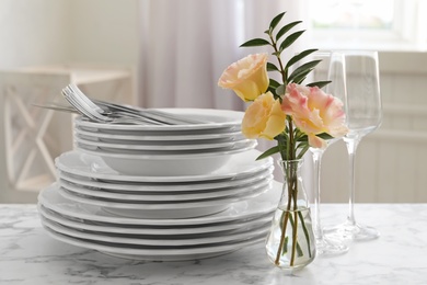 Photo of Set with clean dishes and flowers on white marble  table