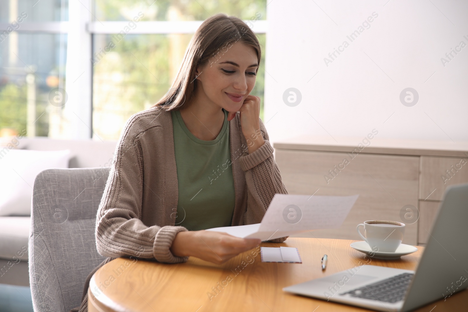 Photo of Woman reading letter at wooden table in room