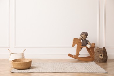 Photo of Rocking horse with bear toy and wicker baskets near white wall in child room. Interior design