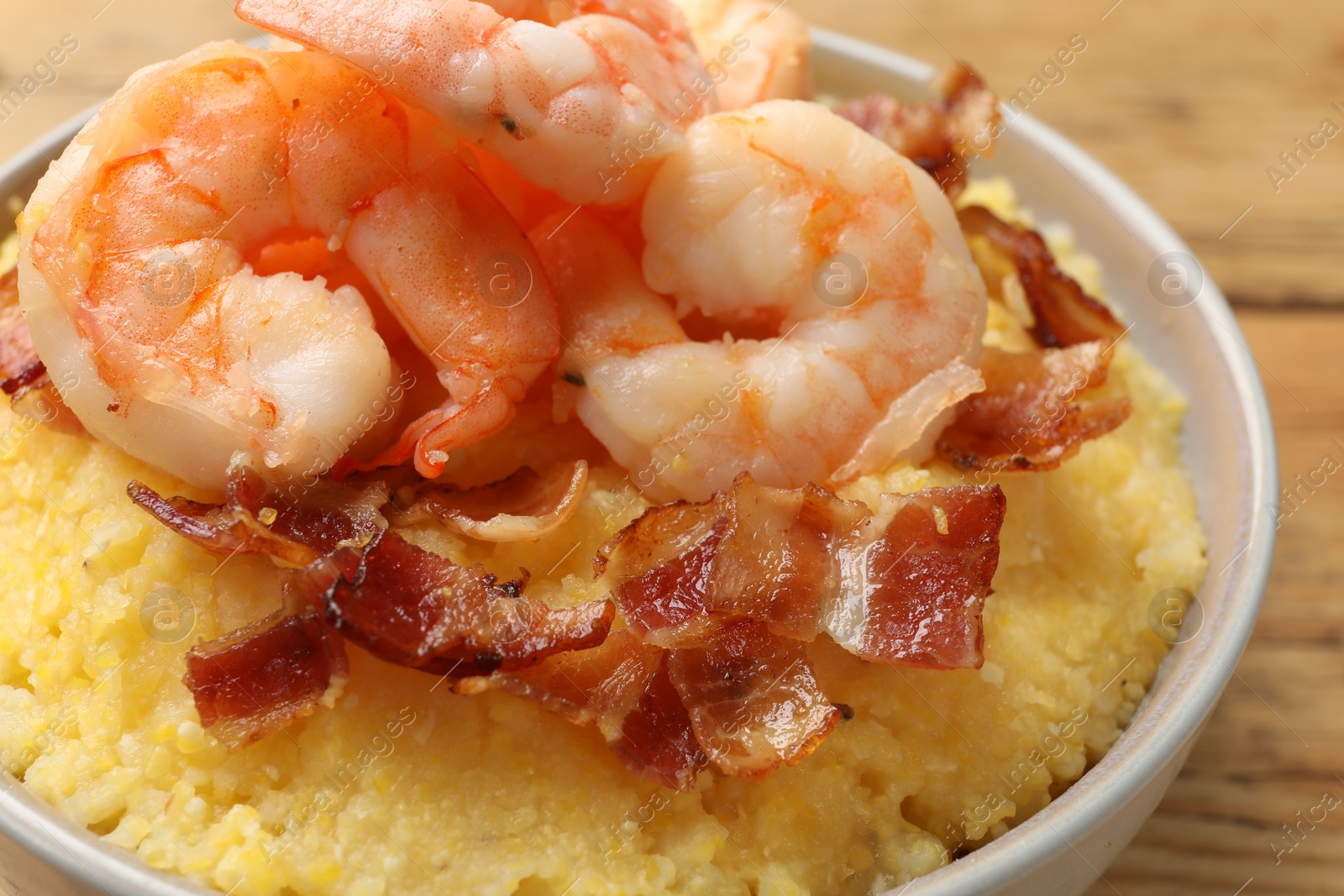 Photo of Fresh tasty shrimps, bacon and grits in bowl on table, closeup