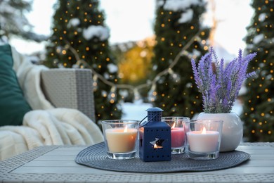 Beautiful burning candles, lantern and potted flowers on table outdoors. Cozy winter