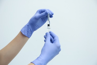 Doctor holding syringe with COVID-19 vaccine on light background, closeup