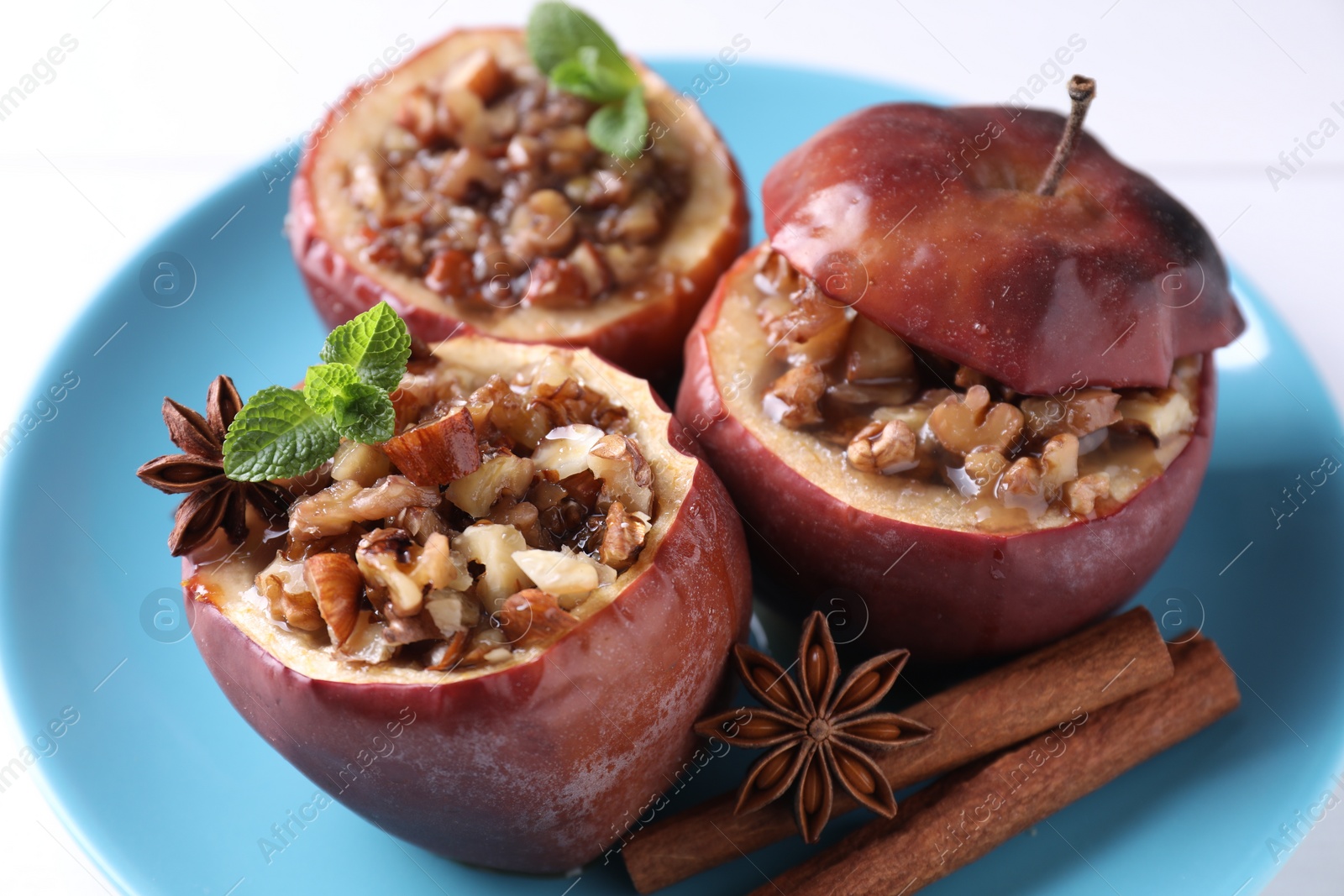 Photo of Tasty baked apple with nuts, honey, spices and mint on white table, closeup