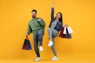 Photo of Excited couple with shopping bags having fun on orange background