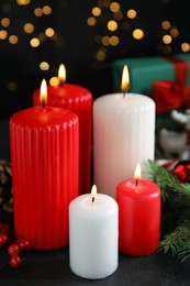 Photo of Burning candles and festive decor on dark table against blurred Christmas lights