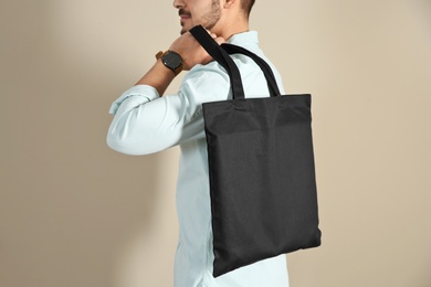 Photo of Young man holding textile bag on color background, closeup. Mockup for design