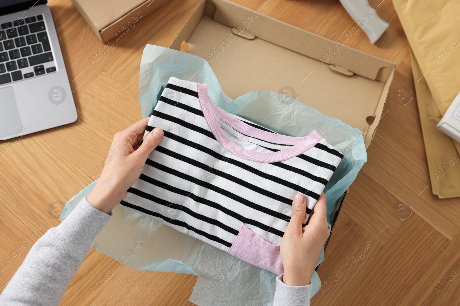 Photo of Woman packing clothes into cardboard box at wooden table, top view. Online store