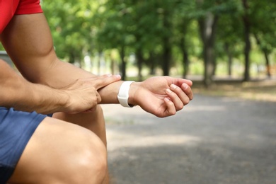 Young man checking pulse after training outdoors, closeup