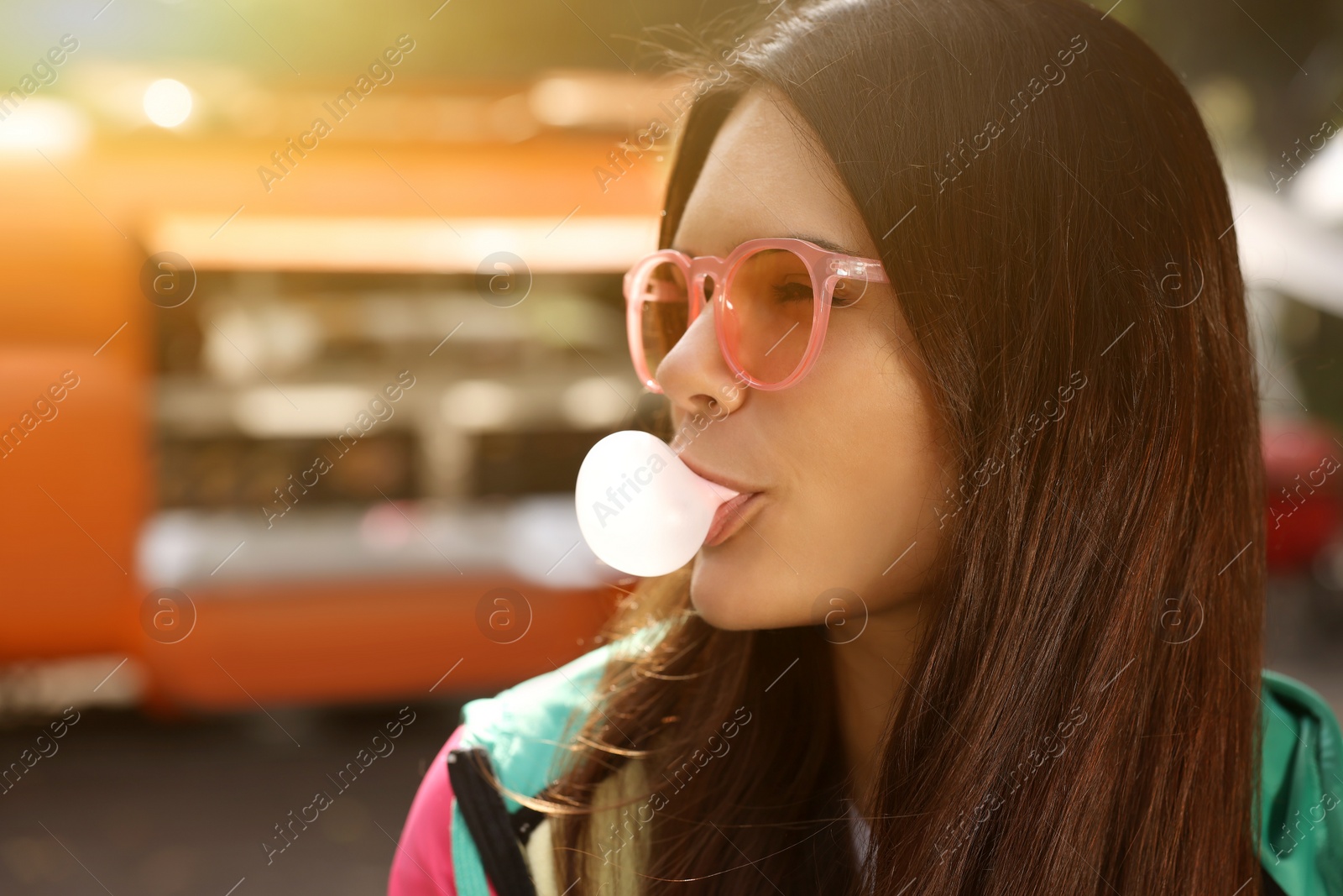 Photo of Beautiful young woman in pink glasses blowing chewing gum outdoors, space for text