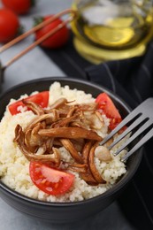 Tasty couscous with mushrooms and tomatoes on grey table, closeup