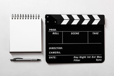 Movie clapper, notebook and pen on light textured background, flat lay