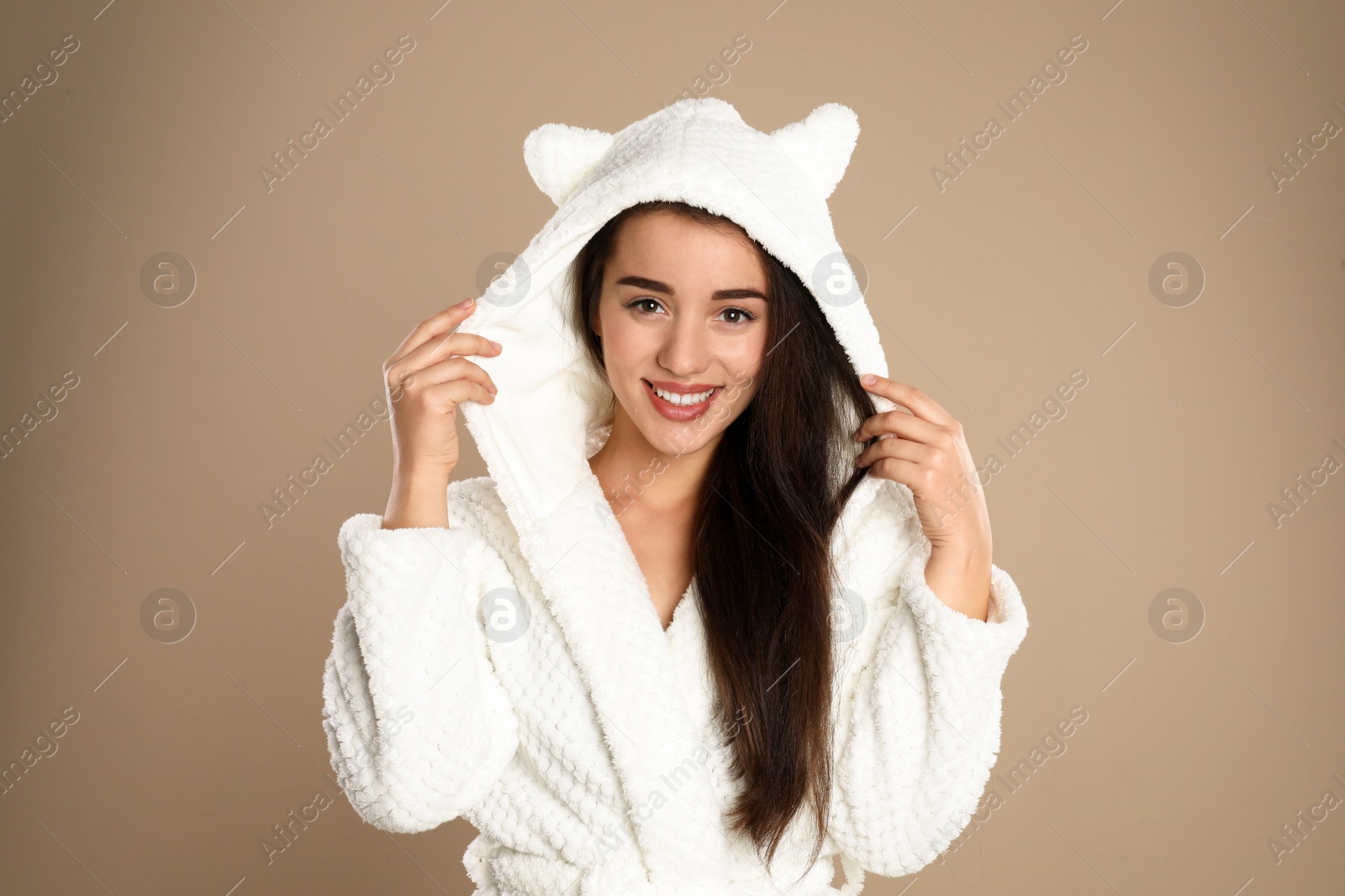 Photo of Beautiful young woman in bathrobe with funny hood on brown background