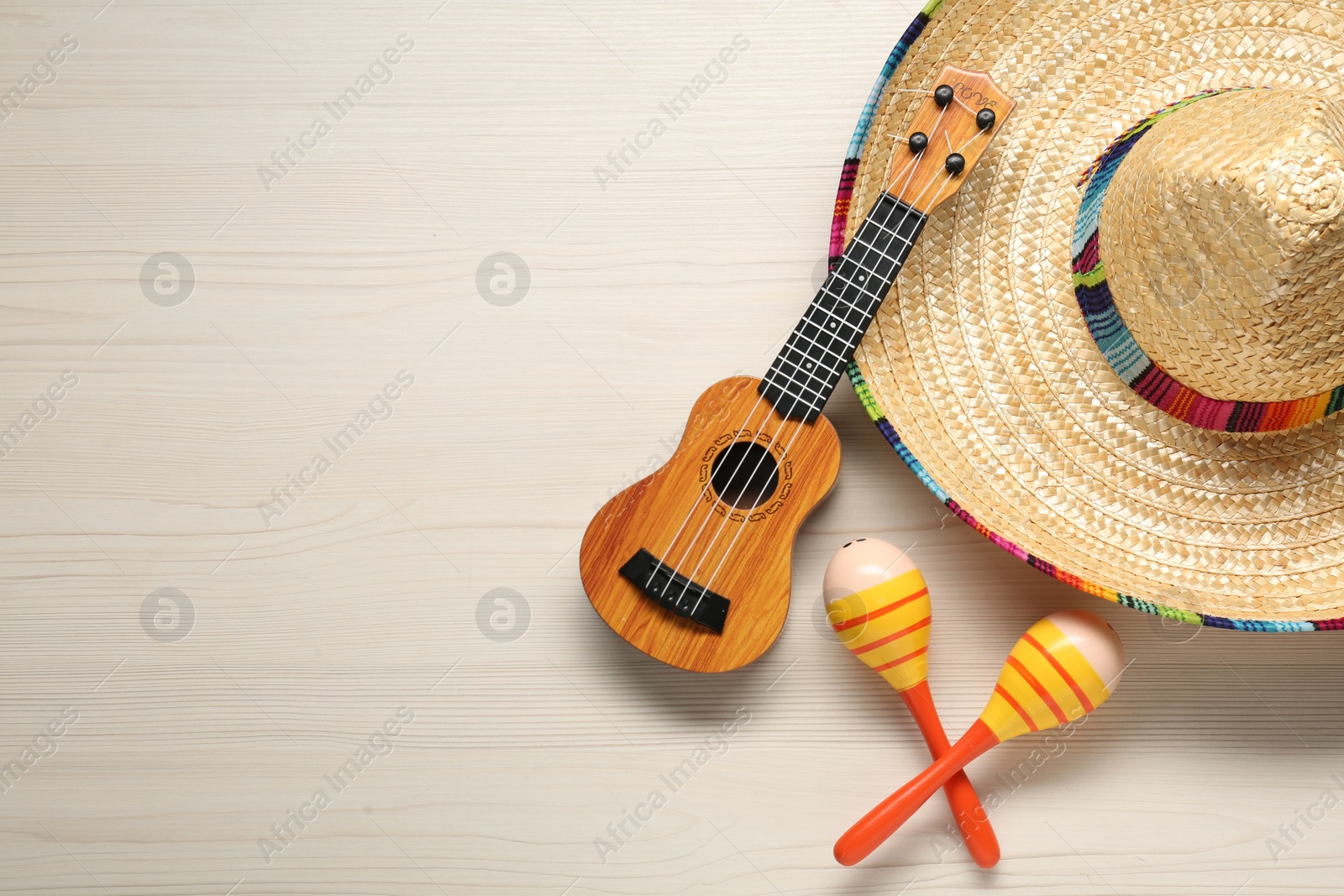Photo of Mexican sombrero hat, maracas and guitar on white wooden background, flat lay. Space for text
