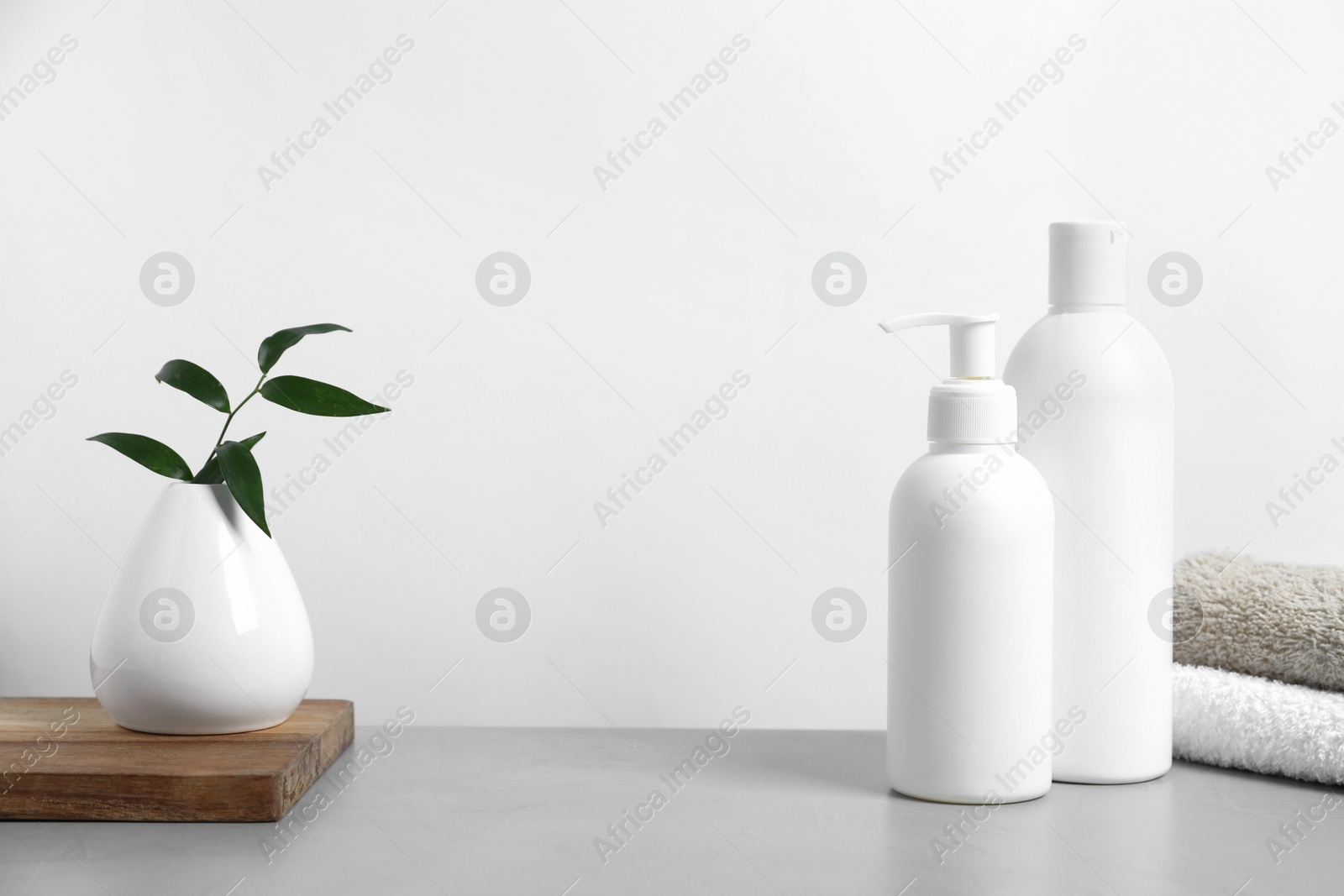Photo of Bottles with different cosmetic products and green leaves in vase on light grey table against white background, space for text
