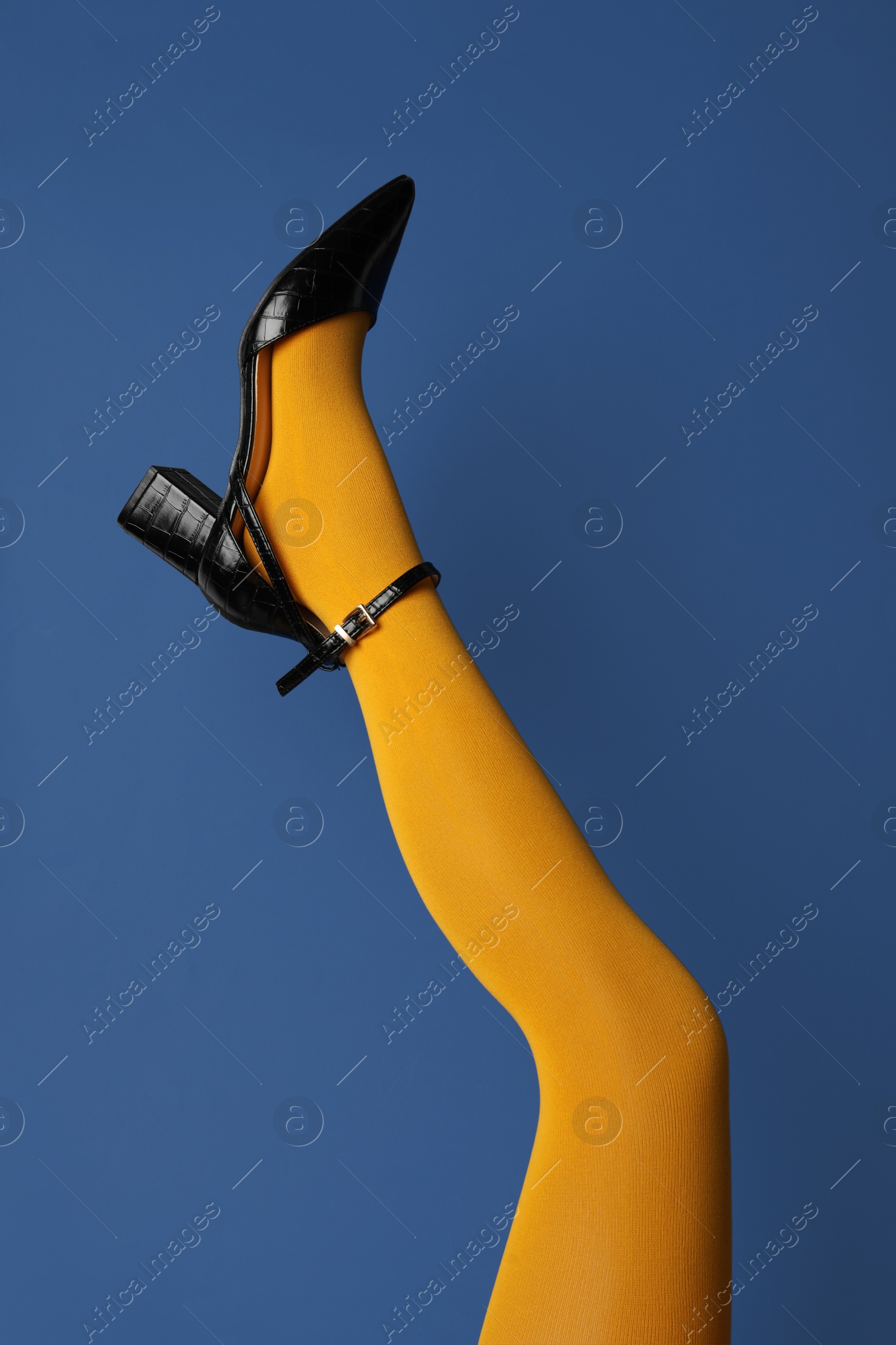 Photo of Woman wearing bright tights and high heel shoe on blue background, closeup