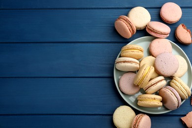Photo of Delicious macarons on blue wooden table, flat lay. Space for text