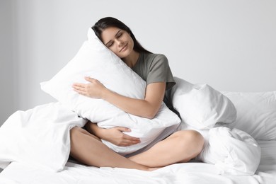 Beautiful young woman hugging pillow on bed at home