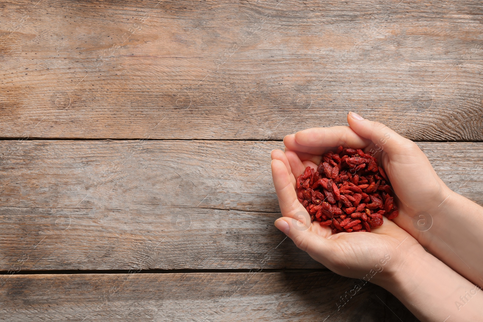 Photo of Woman holding red dried goji berries on wooden background, top view. Space for text
