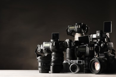 Photo of Modern cameras on white wooden table against dark background. Space for text
