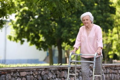 Photo of Elderly woman with walking frame outdoors. Medical help