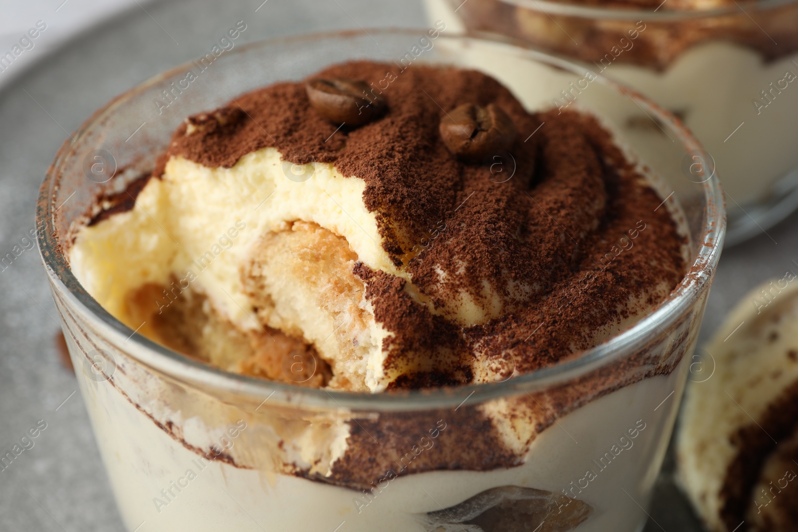 Photo of Delicious tiramisu in glass and coffee beans on table, closeup