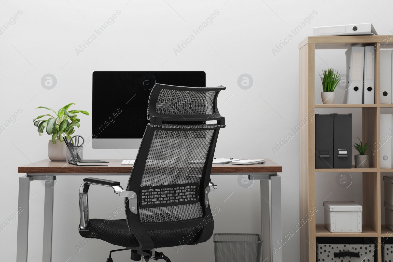 Photo of Cozy workspace with computer on desk, chair and bookcase near white wall at home