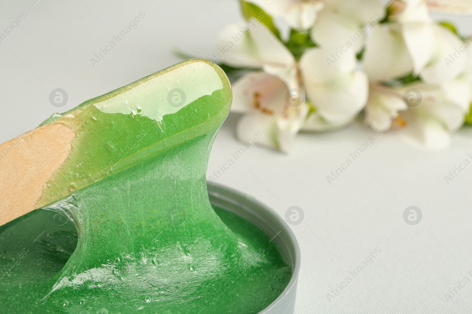 Photo of Wooden spatula and hot depilatory wax on light background, closeup