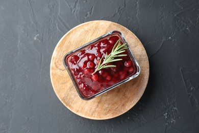 Photo of Fresh cranberry sauce and rosemary in glass bowl on gray textured table, top view