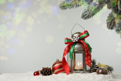 Decorative lantern and Christmas decor on snow against festive lights. Space for text