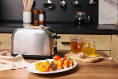 Toaster with roasted bread, tea and sandwiches on wooden table in kitchen. Tasty breakfast