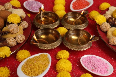 Photo of Diwali celebration. Beautiful composition with tasty Indian sweets and diya lamps on shiny red table