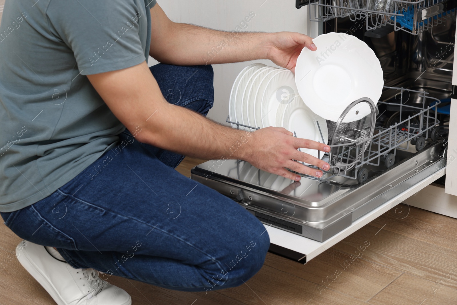 Photo of Man loading dishwasher with plates indoors, closeup