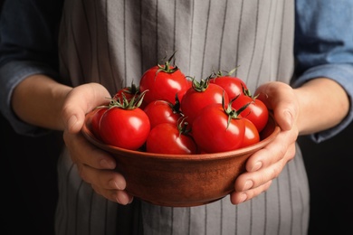 Photo of Woman holding wooden bowl with ripe cherry tomatoes, closeup