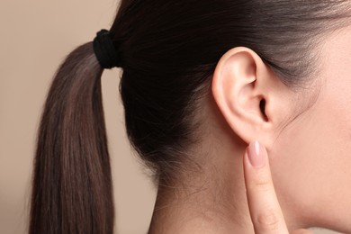 Young woman pointing at her ear on beige background, closeup