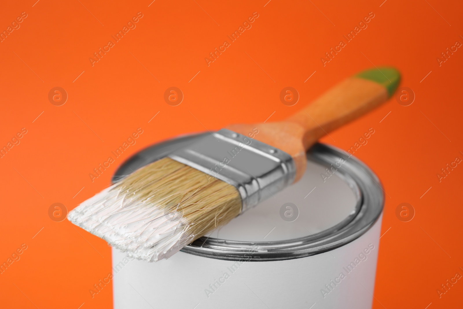 Photo of Can of white paint with brush on orange background