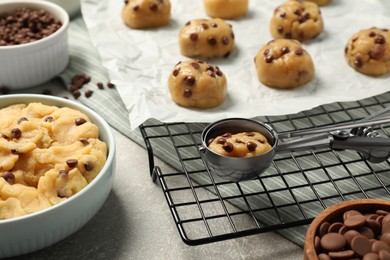 Photo of Bowl with dough and uncooked chocolate chip cookies on light grey table, closeup