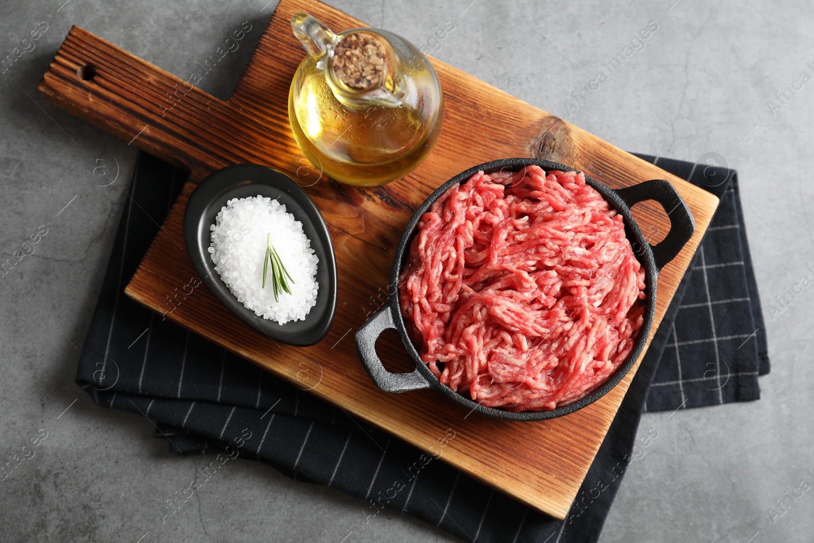 Photo of Raw ground meat in bowl, salt and oil on grey table, top view