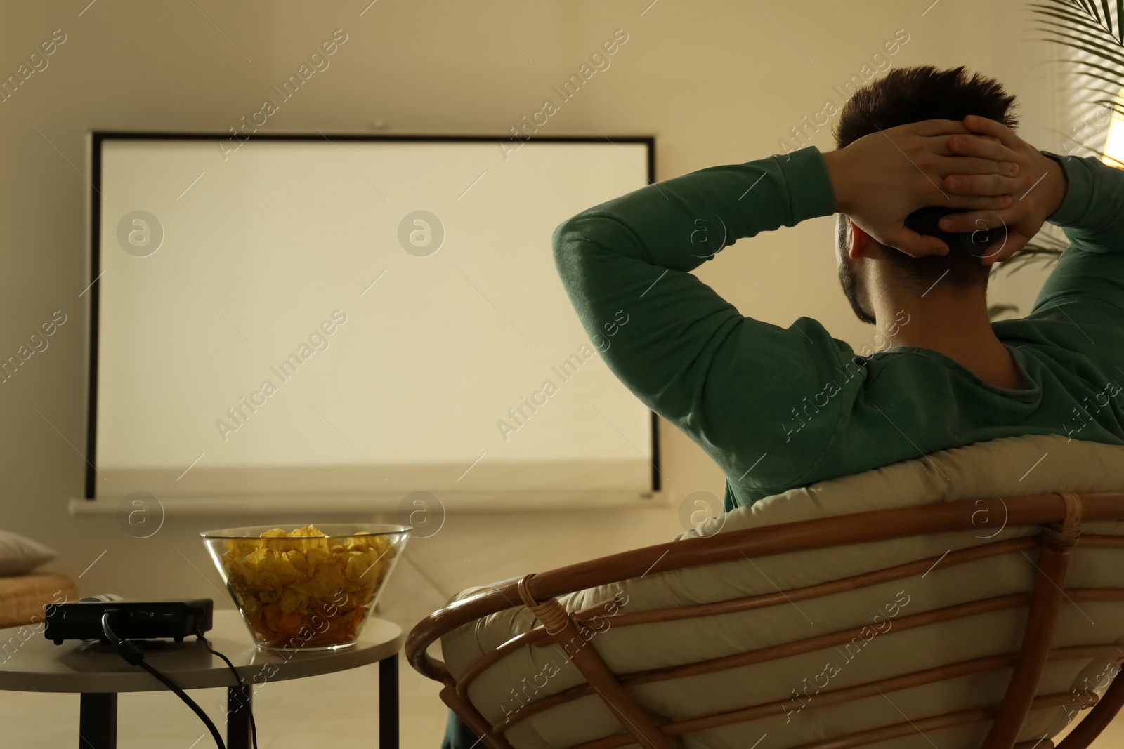 Photo of Young man watching movie using video projector at home
