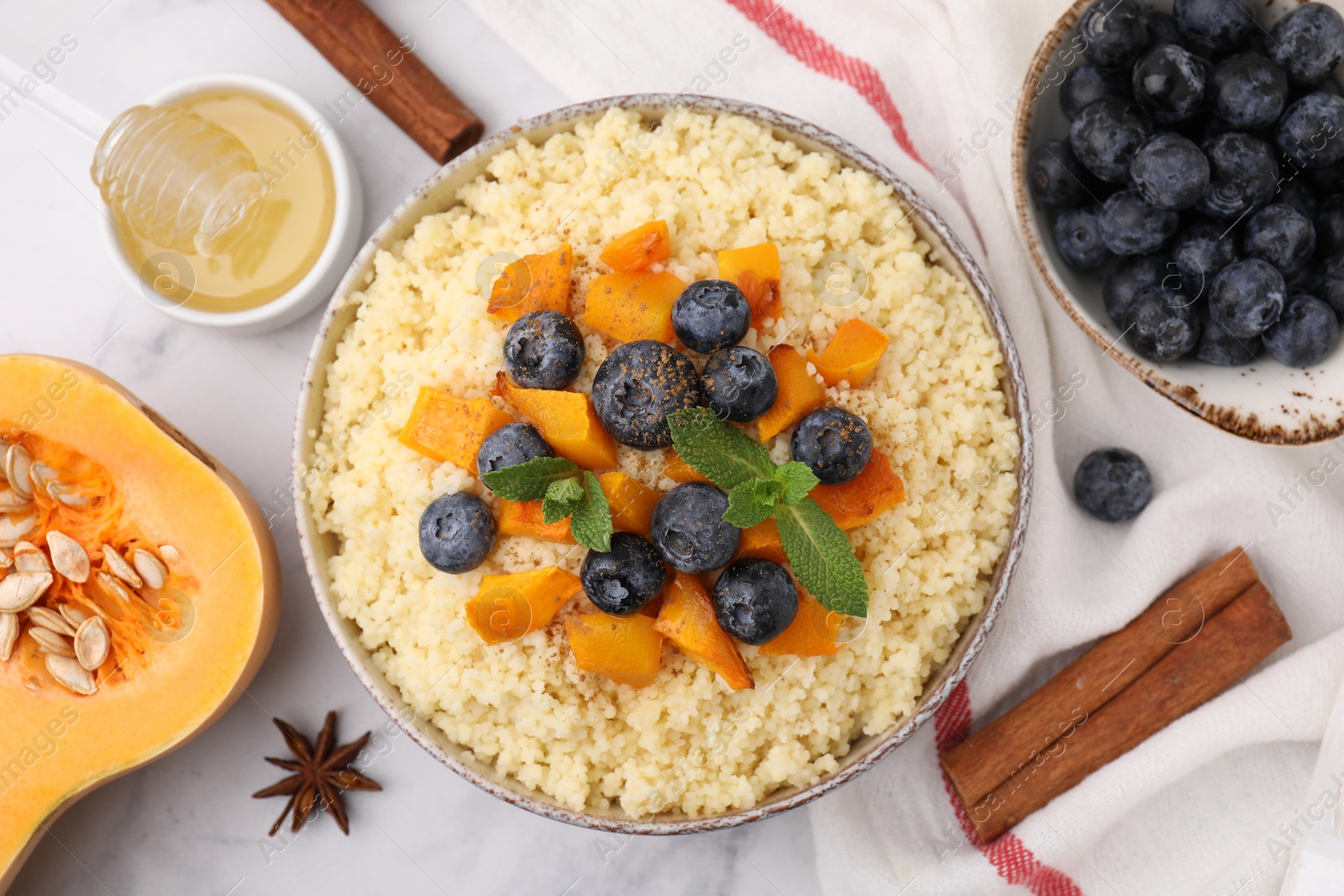 Photo of Bowl of tasty couscous with blueberries, pumpkin, ingredients on white table, flat lay