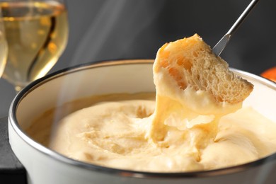 Photo of Dipping piece of bread into fondue pot with melted cheese on grey background, closeup