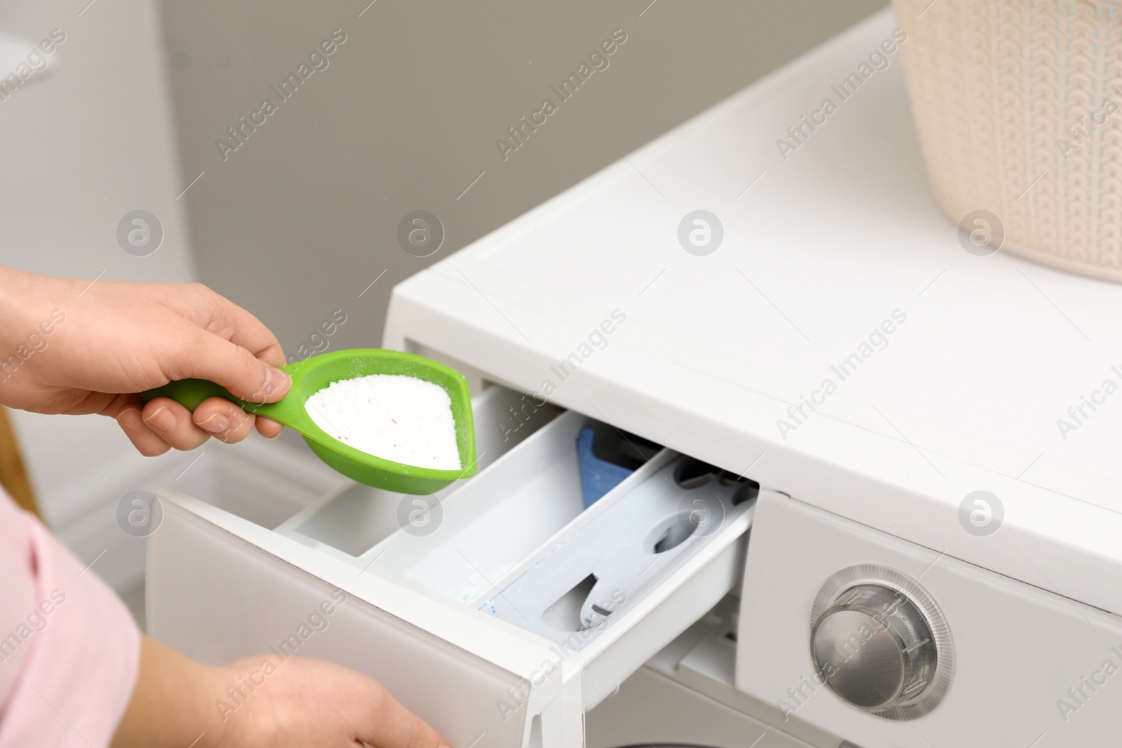 Photo of Woman pouring powder into drawer of washing machine in laundry room, closeup