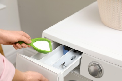 Woman pouring powder into drawer of washing machine in laundry room, closeup