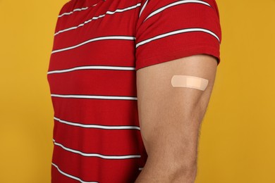 Photo of Vaccinated man with medical plaster on his arm against yellow background, closeup