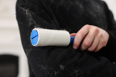 Photo of Pet shedding. Man with lint roller removing dog's hair from sweater indoors, closeup