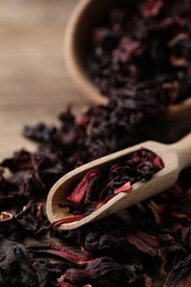 Photo of Wooden scoop with dry hibiscus tea on table, closeup